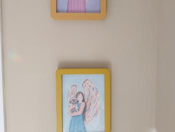 Two paintings of angels in frames holding onto a Lhasa Apso and Springer Spaniel dog.