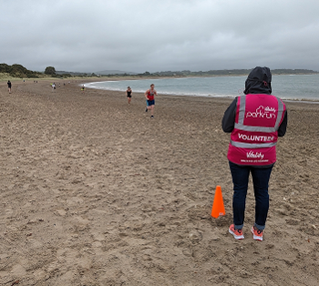 A parkrun volunteer looks across a beach towards runners who are about to finish.