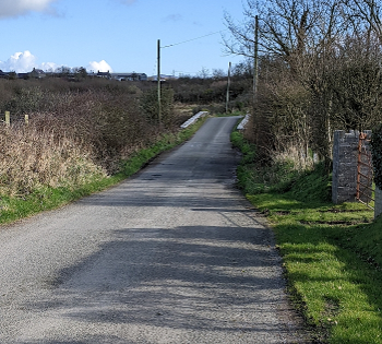 A country lane in NW Wales. Telegraph poles and a bridge over a stream in the distance.