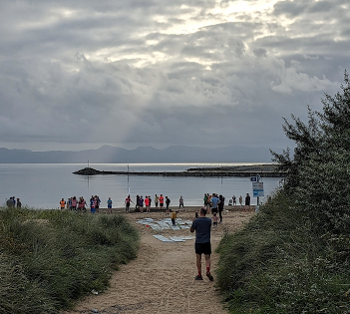 People gather on the beach for parkrun. A crepuscular ray picks out the breakwater's end.