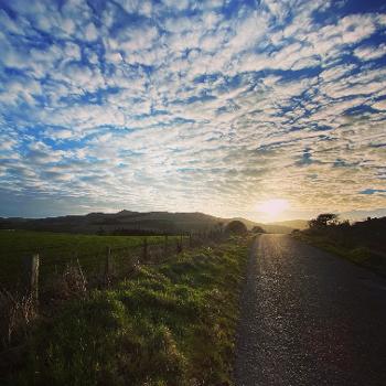 Country lane with the sun rising over hills with blue sky and dabbled clouds 
