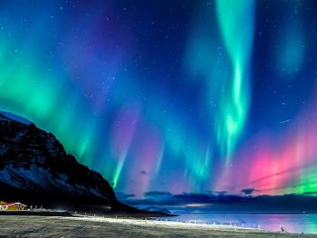 The Northern Lights over a beach in Iceland, shining green, blue and pink
