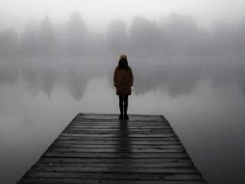 black and white photo of a girl standing on a jetty in the fog
