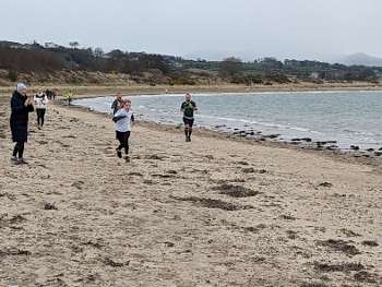 Runners spread into the distance along a yellow sandy beach,  approaching parkrun finish.