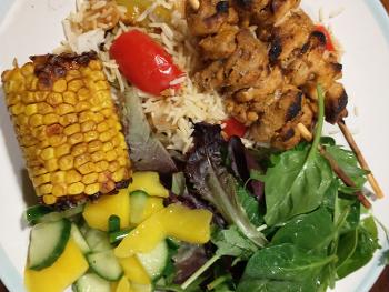 Image shows chicken skewers with rice, salad and sweetcorn