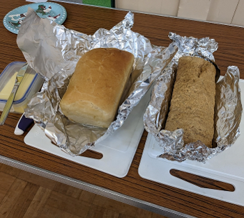 Two loaves of bread unwrapped from foil, sitting on cutting boards. A butter tub to left.