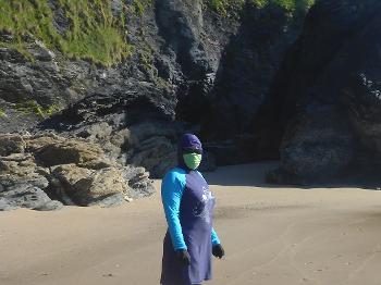 figure on a beach in a blue burkini with green face cover and dark glasses