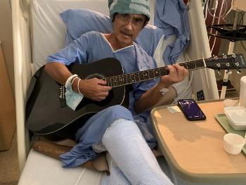 Man in hospital bed with guitar, resting after deep brain stimulation surgery.